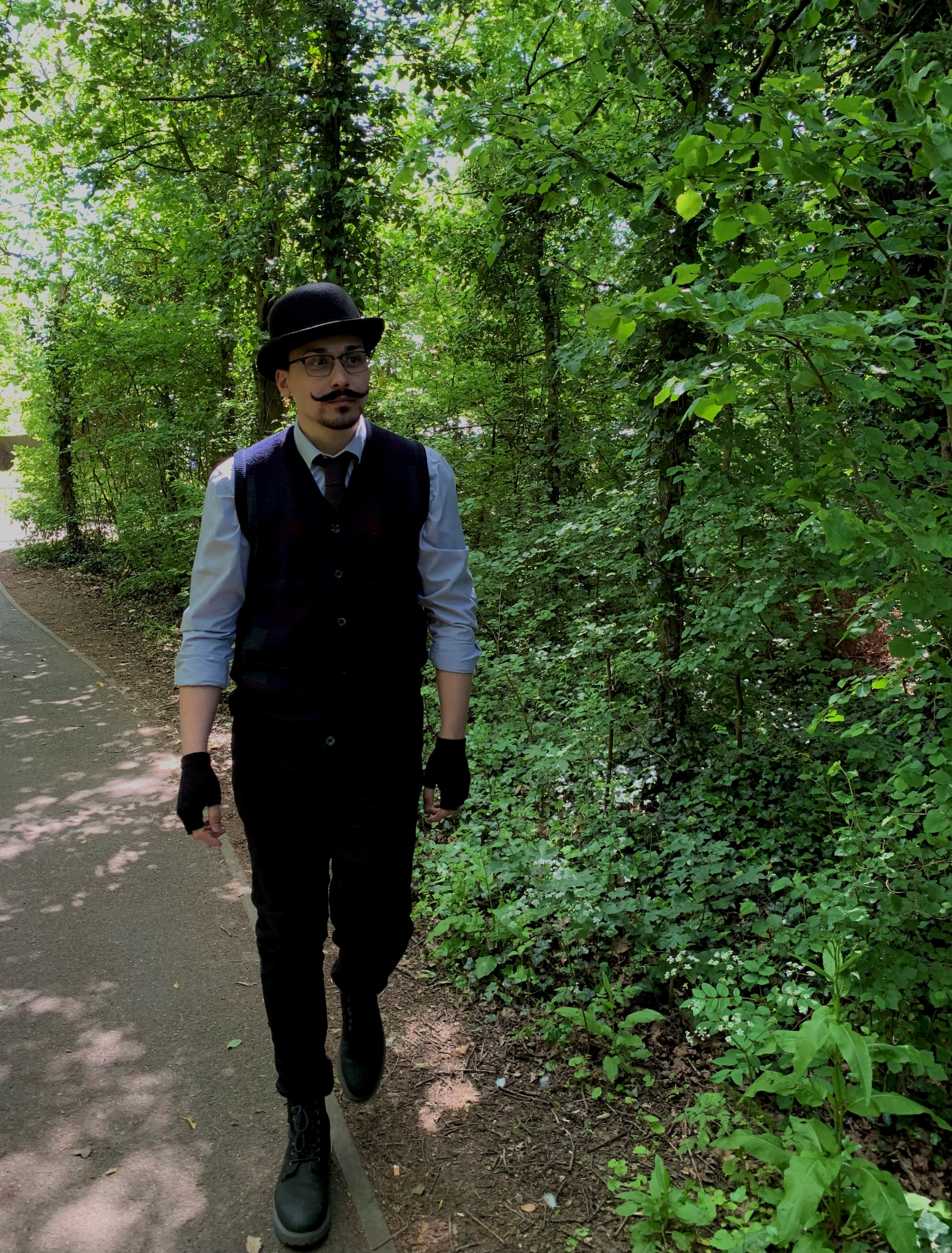 J. D. Dixon, a man in a bowler hat and suit, walks through a woodland